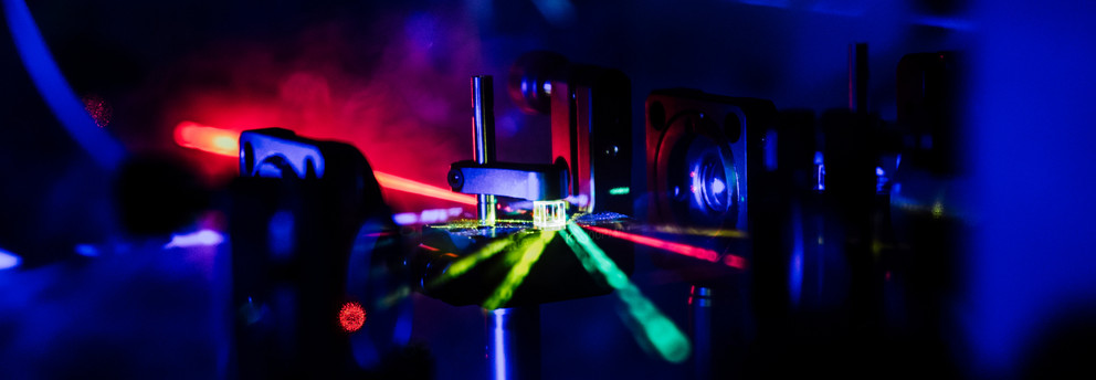 Strahlteilerwürfel mit Laserstrahlen Das Bild zeigt mehrere, unterschiedlich farbige Laserstrahlen, die auf einen Strahlteilerwürfel treffen.